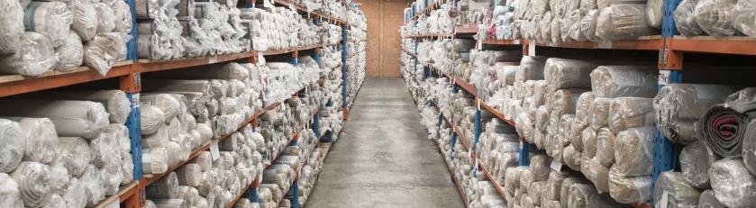 Many rolls of carpet are stacked neatly on warehouse carpet racks.